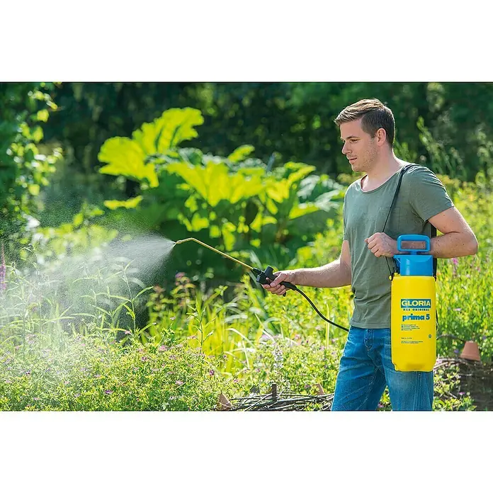 Gloria Drucksprühgerät Prima 5 mit Messing-Lanze & -Düse - 5 l - Mann benutzt eine Gloria Prima 5 Druckspritze im Garten, um Pflanzen zu pflegen. Das gelb-blaue Gerät ist mit einem Tragegurt ausgestattet.