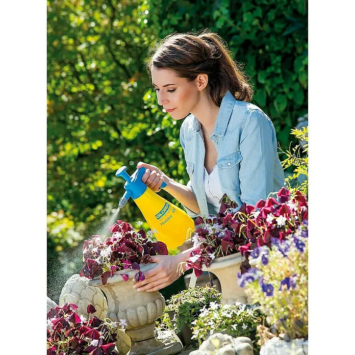 Gloria Drucksprühgerät Hobby 100 mit verstellbarer Düse - 1 l - Frau bewässert Pflanzen mit einer gelben Gloria Hobby 100 Drucksprühflasche, ideal für Gartenarbeit und Pflanzenpflege.