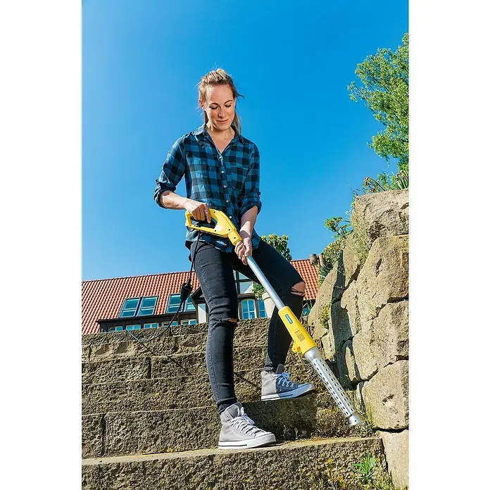 Gloria Unkrautvernichter Thermoflamm bio Electro - 2.000 W, Flammtemperatur: 650 °C - Eine Frau benutzt einen gelben GLORIA Thermoflamm bio Elektro-Unkrautvernichter auf einer Steintreppe mit blauem Himmel im Hintergrund.