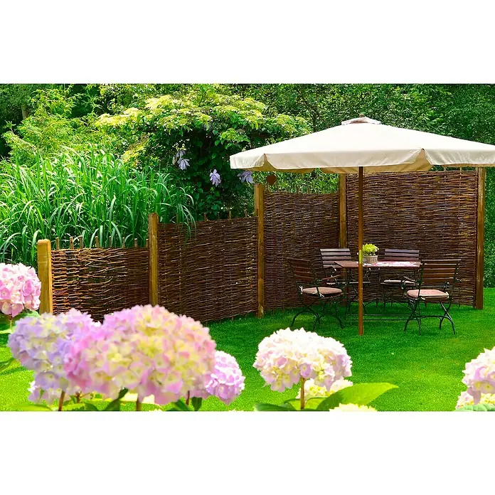 T & J Sichtschutzelement Aso - 180 x 150 cm, Braun - Entspannender Gartenbereich mit einem charmanten Flechtzaun, einem einladenden Gartentisch mit Sonnenschirm und blühenden Hortensien.