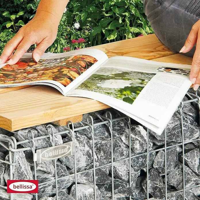 Bellissa Gabionenbank - 100 x 30 x 46 cm, Metall, Maschenbreite: 50 mm, Maschenhöhe: 100 mm - Eine Person sitzt auf einer Bellissa Gabione mit Holzauflage und liest eine Zeitschrift im Garten.