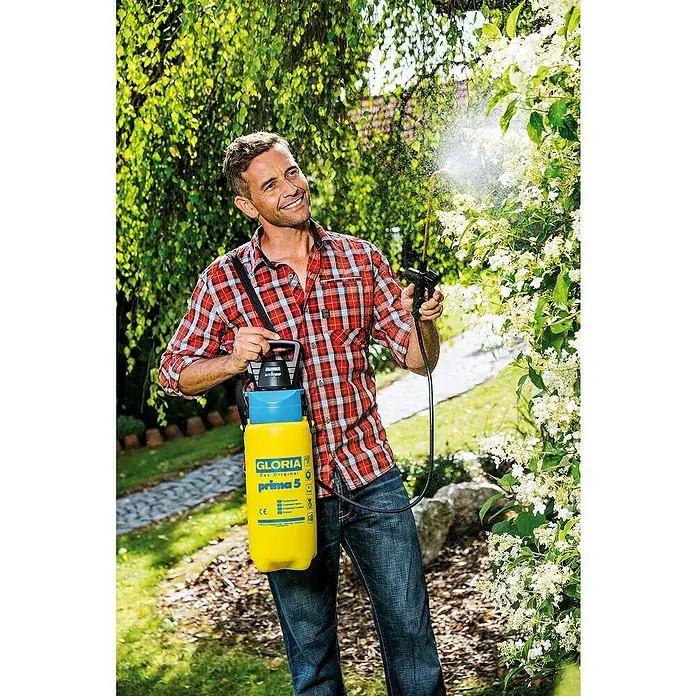 Gloria Drucksprühgerät AutoPump Set mit Batterie-/Akku-Betrieb - 5 l, Mit Tragegurt - Ein Mann benutzt einen GLORIA Prima 5 Drucksprüher, um Pflanzen zu besprühen. Das Gerät ist gelb und blau und wird über der Schulter getragen.