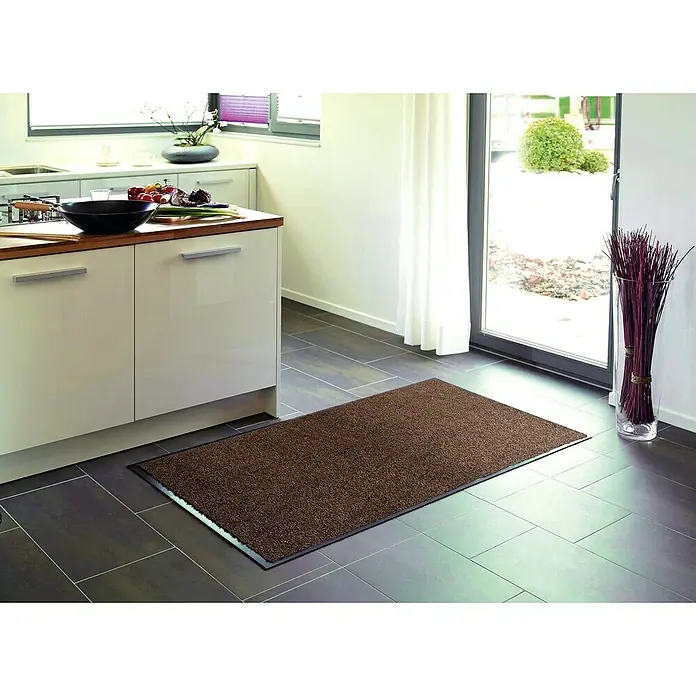Astra Schmutzfangmatte Proper Tex - Braun, 60 x 90 cm, Material Nutzschicht: 100 % Polyamid - Braune Schmutzfangmatte mit schwarzem Rand auf grauem Fliesenboden in einer modernen Küche, ideal für Sauberkeit und Stil im Eingangsbereich.
