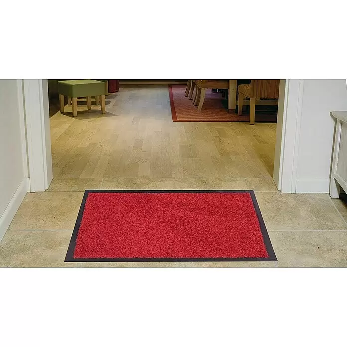 Astra Schmutzfangmatte Proper Tex - Rot, 60 x 180 cm, Material Nutzschicht: 100 % Polyamid - Rote flauschige Fußmatte mit dunklem Rand, auf Fliesenboden in einer Türöffnung, die zu einem Raum mit Holzboden führt.
