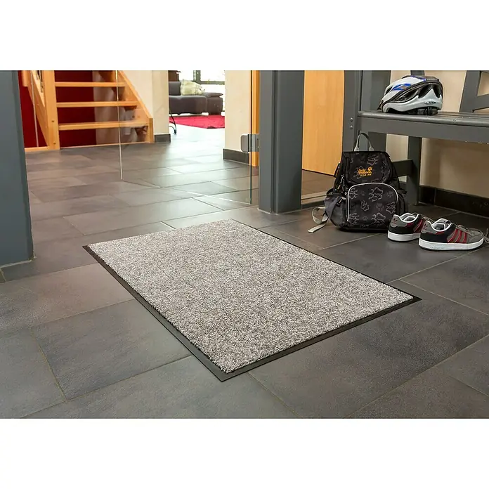 Astra Schmutzfangmatte Proper Tex - Grau, 60 x 180 cm, Material Nutzschicht: 100 % Polyamid - Ein grauer Schmutzfangläufer liegt auf einem gefliesten Boden, neben einer Bank mit einem Rucksack, einem Helm und Schuhen.