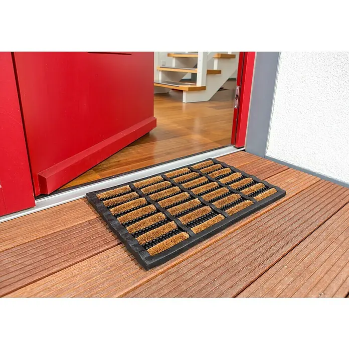 Astra Fußmatte RiminiSchwarz/Natur, 40 x 60 cm, 70% Kokos, 30 % Gummi - Fußmatte vor einer offenen roten Tür. Die Matte ist aus Kokosfasern und Gummi gefertigt. Sie liegt auf einem Holzboden.