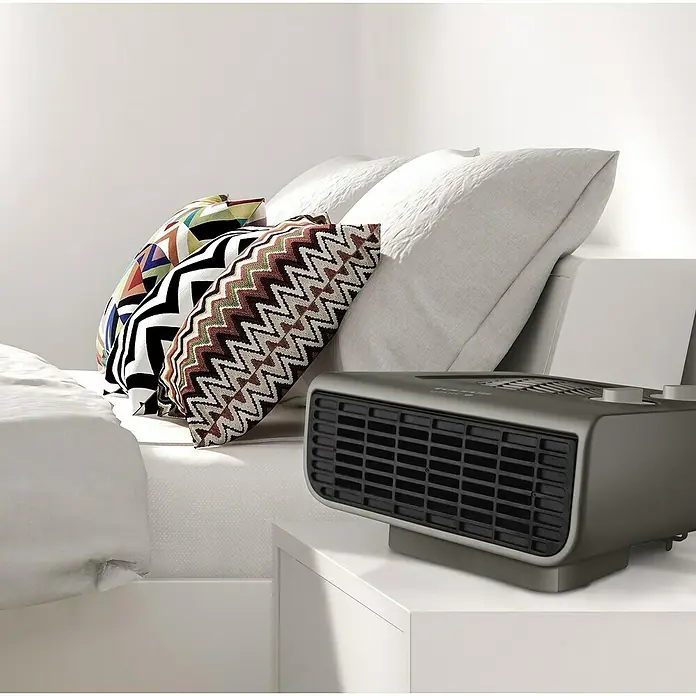 Taurus Calefactor de aire Java - 1.000 kW - 2.000 kW, Gris - Un calentador portátil gris está sobre una mesita de noche, al lado de una cama con almohadas. Ideal para horas acogedoras.