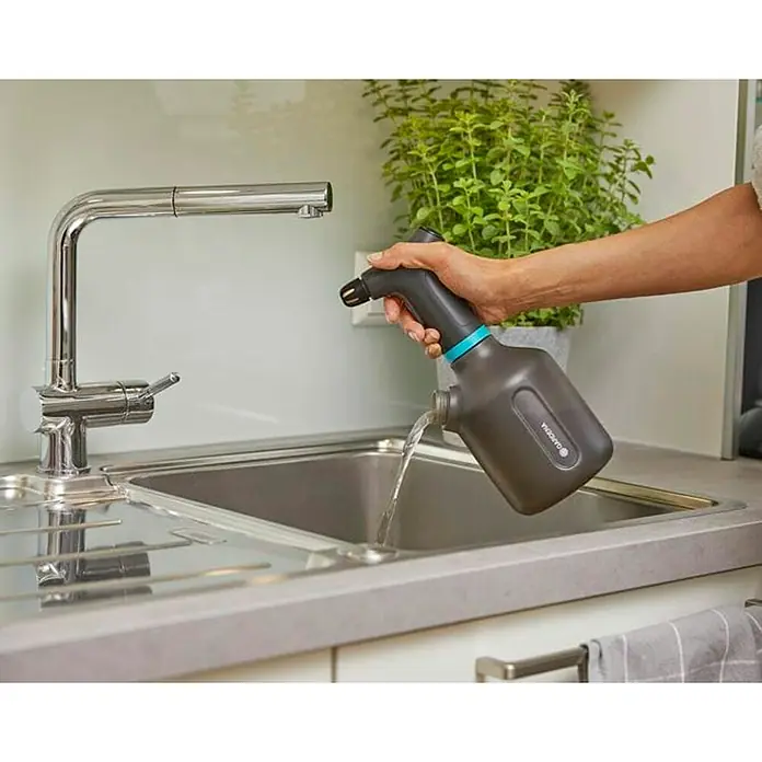 Gardena Handsprüher Easy Pump1 l - Eine Person füllt eine Gardena-Pflanzenspritze an einem Wasserhahn in einer Spüle auf. Die Spritze ist grau mit einem blauen Akzent.