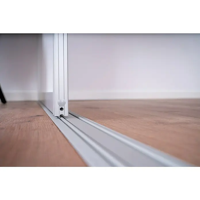 Room Plaza Easy Doing Schiebetür-Bau-Set - Ahorn Naturwuchs, Farbe Beschlag: Silber - Detailaufnahme einer silbernen Schiebetürschiene auf einem Holzboden vor einer weißen Wand. Fokus liegt auf der Konstruktion und dem Material.
