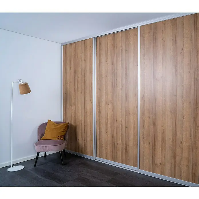 Room Plaza Easy Doing Schiebetür-Bau-Set - Eiche Country, Farbe Beschlag: Silber - Eine moderne Inneneinrichtung mit einem stilvollen Kleiderschrank mit Holzoptik und Schiebetüren neben einem Sessel und einer Lampe.