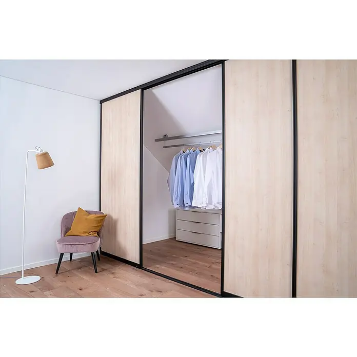 Room Plaza Easy Doing Schiebetür-Bau-Set - Ahorn Naturwuchs, Farbe Beschlag: Schwarz - Holzschrank mit Schiebetüren und schwarzem Rahmen, der einen Blick auf Kleidung und Kommode im Schrankinneren freigibt, neben einem Stuhl.