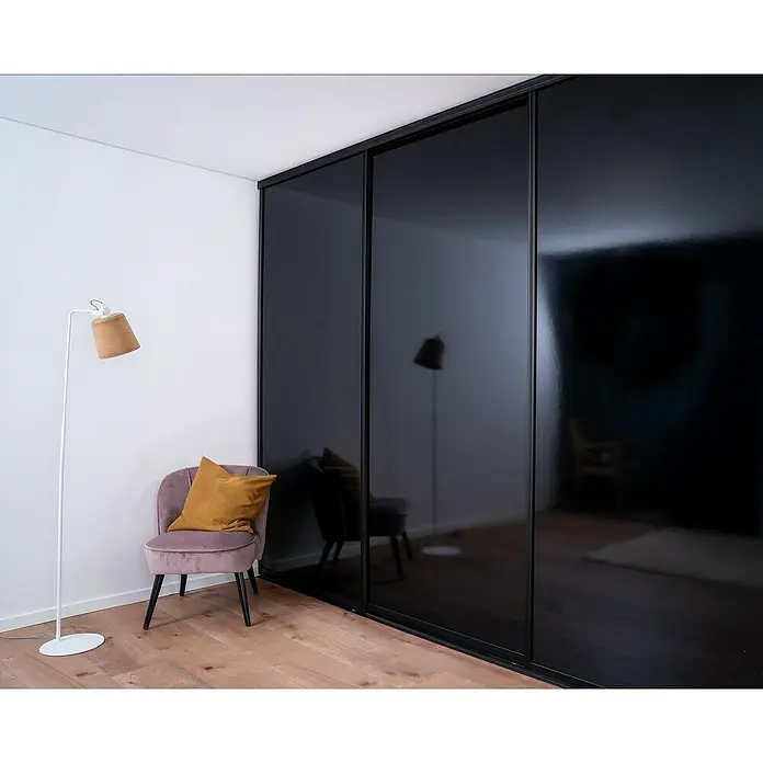Room Plaza Easy Doing Schiebetür-Bau-Set - Hochglanz Schwarz/Hochglanz Weiß, Farbe Beschlag: Schwarz - Ein elegantes Zimmer mit einem stilvollen, schwarzen Schiebetürenschrank, einem Sessel mit Kissen und einer Stehlampe.