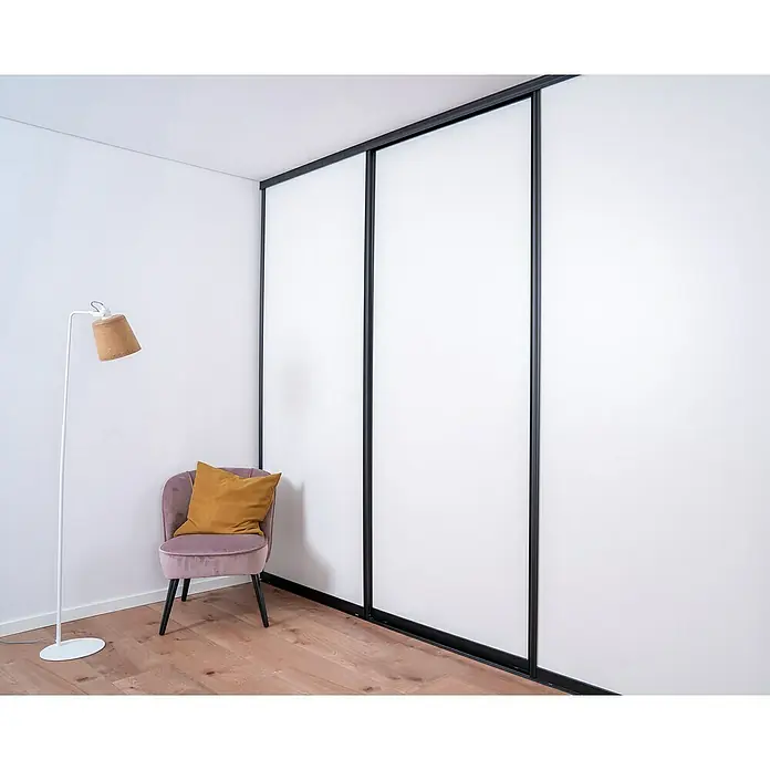 Room Plaza Easy Doing Schiebetür-Bau-SetSignalweiß, Profilfarbe: Schwarz - Elegantes Zimmer mit weißem Kleiderschrank mit Schiebetüren und einem modernen Lesesessel mit Lampe.