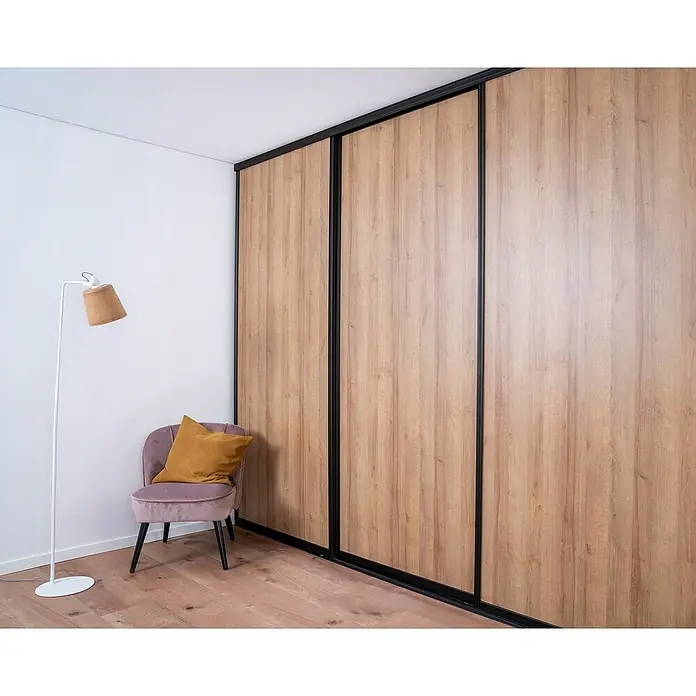 Room Plaza Easy Doing Schiebetür-Bau-Set - Eiche Country, Farbe Beschlag: Schwarz - Eleganter Kleiderschrank mit Holzstruktur und schwarzen Akzenten, ergänzt durch einen stilvollen Sessel und eine Stehlampe.