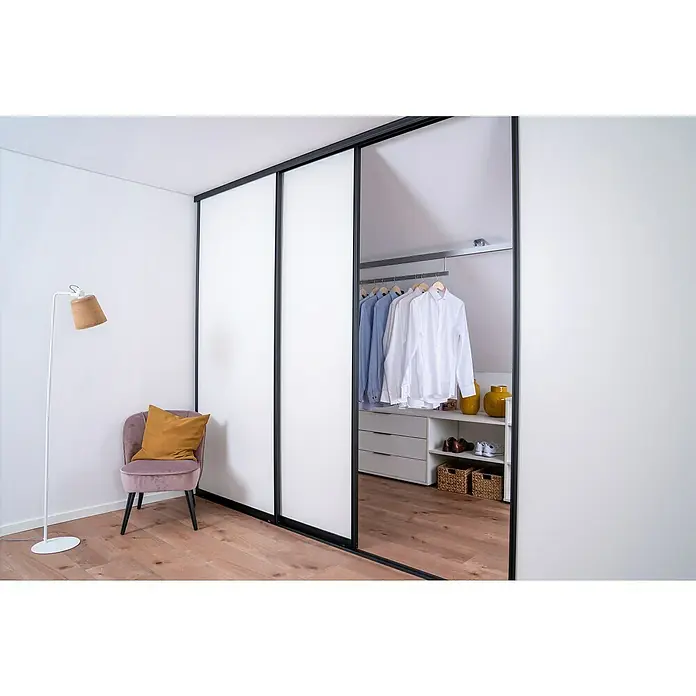 Room Plaza Easy Doing Schiebetür-Bau-SetSignalweiß, Profilfarbe: Schwarz - Schlafzimmer-Interieur mit einem Schiebetürenschrank, der begehbaren Kleiderschrank freigibt, einem Sessel und einer Stehlampe.