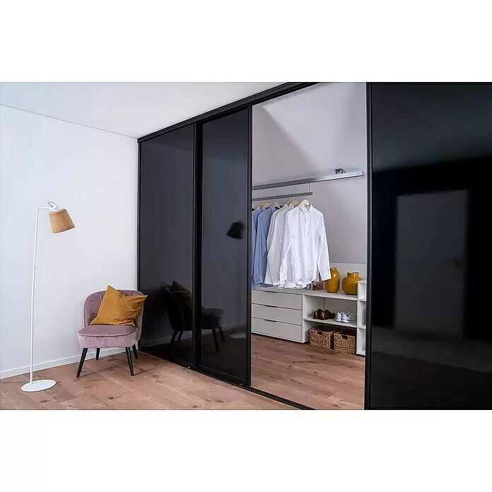 Room Plaza Easy Doing Schiebetür-Bau-Set - Hochglanz Schwarz/Hochglanz Weiß, Farbe Beschlag: Schwarz - Moderner Kleiderschrank mit schwarzen Schiebetüren, eine Tür offen mit Kleidung, Regalen und Schuhen, neben Stuhl und Lampe.