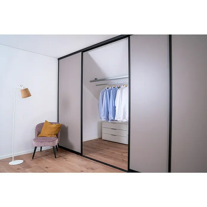 Room Plaza Easy Doing Schiebetür-Bau-Set - Taupe, Farbe Beschlag: Schwarz - Ein modernes Schlafzimmer mit einem Schiebetürenschrank, einem eleganten Sessel und einer Stehlampe, die eine gemütliche Atmosphäre schaffen.