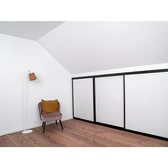 Room Plaza Easy Doing Schiebetür-Bau-Set Kniestock - Reinweiß Miniperl, Farbe Beschlag: Schwarz - Helles Interieur mit großem Schrank mit Schiebetüren, Sessel und Stehlampe. Der geräumige Kleiderschrank bietet viel Stauraum.