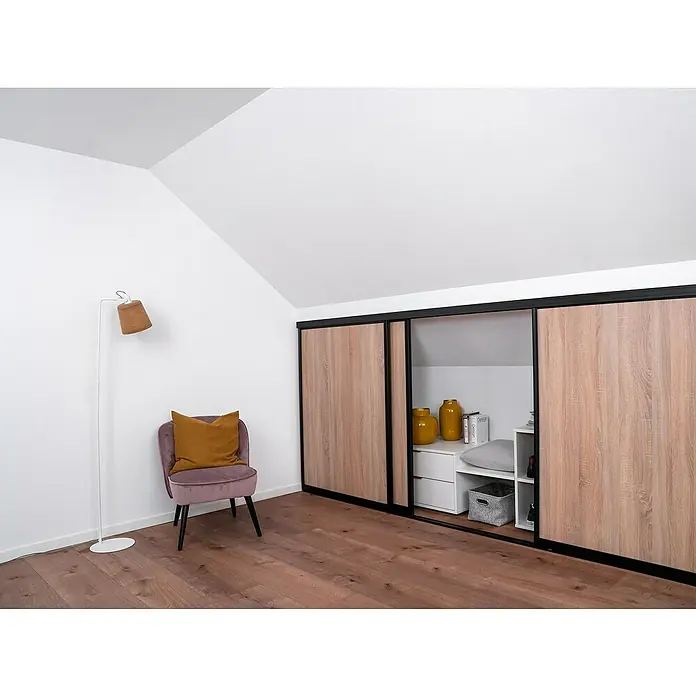 Room Plaza Easy Doing Schiebetür-Bau-Set KniestockEiche geplankt, Profilfarbe: Schwarz - Gemütliches Dachzimmer mit einem Kleiderschrank in Holzoptik, einem Sessel mit Kissen und einer Stehlampe, die eine warme Atmosphäre schaffen.