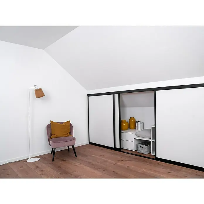 Room Plaza Easy Doing Schiebetür-Bau-Set KniestockReinweiß Miniperl, Profilfarbe: Schwarz - Blick in ein Dachzimmer mit einem Schrank mit Schiebetüren, einem Sessel und einer Stehlampe, die eine gemütliche Atmosphäre schaffen.