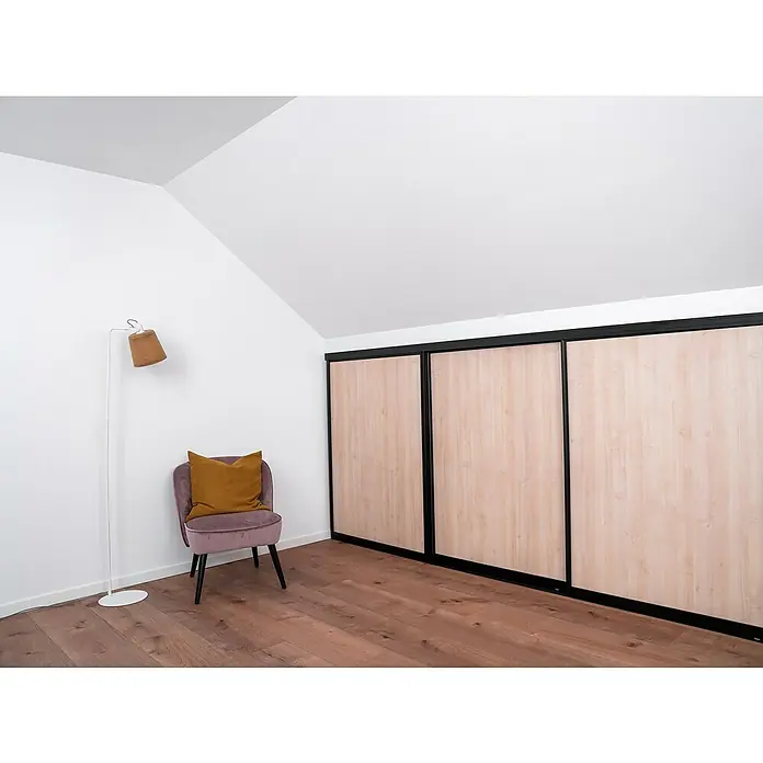 Room Plaza Easy Doing Schiebetür-Bau-Set Kniestock - Ahorn Naturwuchs, Farbe Beschlag: Schwarz - Zimmer mit Schiebetürenschrank, Lampe und Sessel. Der Schrank hat Holzfronten und schwarze Rahmen. Das Zimmer hat einen Holzboden und weiße Wände.