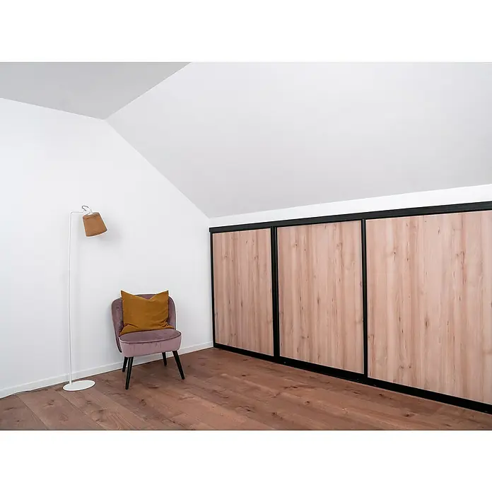 Room Plaza Easy Doing Schiebetür-Bau-Set Kniestock - Buche Naturwuchs, Farbe Beschlag: Schwarz - Einladender Dachbodenraum mit einem eleganten rosa Sessel, einer Stehlampe und einem großen Kleiderschrank mit Holzpaneelen unter einer sanften Dachschräge.