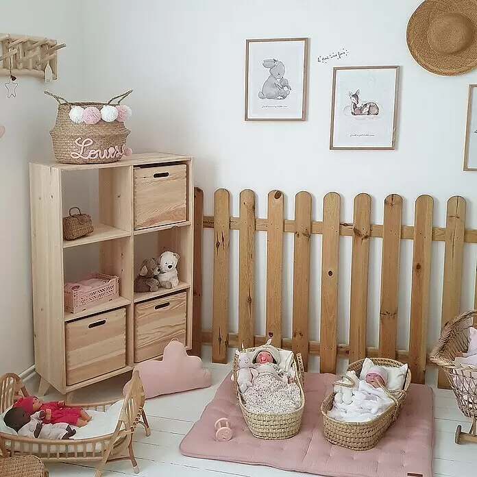 Astigarraga Dinamic Holzregal - H x B x T: 105,4 x 70,8 x 33 cm, Traglast pro Boden: 50 kg, Anzahl Böden: 4 Stk., Schrauben, Natur - Ein gemütliches Kinderzimmer mit Holzregal, Dekozaun und Puppen in geflochtenen Wiegen auf einer rosa Spielmatte.
