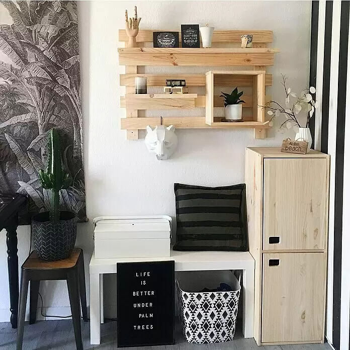 Astigarraga Dinamic Schrank - L x B x H: 33 x 37,3 x 105,4 cm, Kiefernholz - Gemütlich eingerichteter Eckbereich mit hellem Holzpaletten-Wandregal, Naturholzschränken und Bank, dekoriert mit Pflanzen und schwarzer Buchstabentafel.