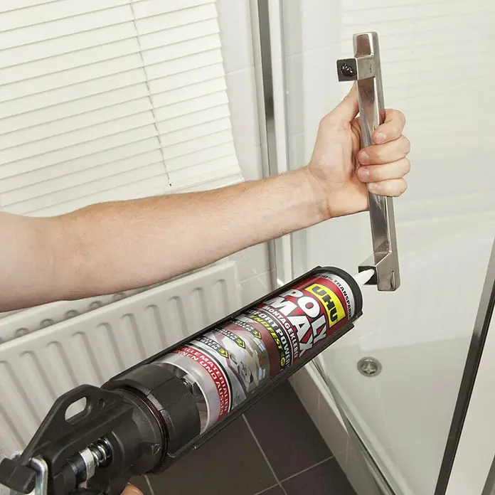 UHU Poly Max Montagekleber Sofort Power - Transparent, 300 g, Kartusche - Eine Kartusche UHU montiert mit einer Pistole, um einen Metallgriff an einer Duschkabine zu befestigen.