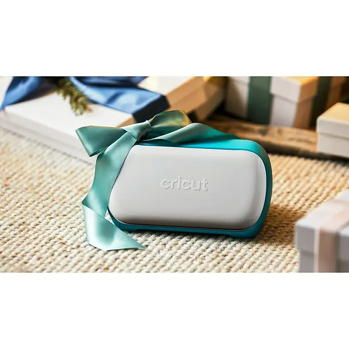 Cricut Joy Schneideplotter Smarte Schneide- und Zeichenmaschine - Türkis/Weiß, Bluetooth, Schnittbreite: 10,4 cm, Schnittlänge: 1,2 m - Ein Cricut Joy Bastelmaschine, verpackt mit einer Schleife, umgeben von Geschenken, perfekt für kreative Projekte.