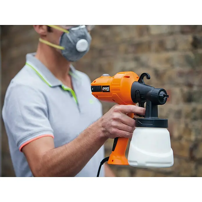 Sistema de pulverización de pintura Paint Sprayer - 400 W, Caudal: 0,5 l/min - Un hombre con máscara sostiene un pulverizador de pintura naranja, ideal para pintar y hacer acabados.
