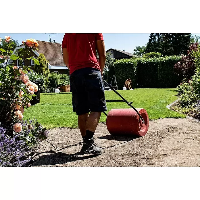 Gardol Rasenerde - 40 l - Eine Person benutzt eine rote Gartenwalze auf einem Schotterweg im Garten.
