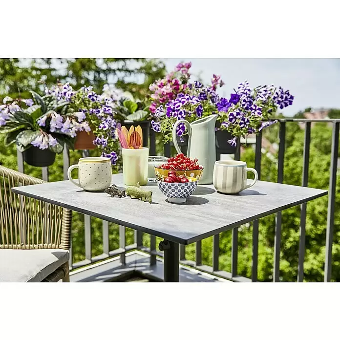 Sunfun Melina Balkontisch - L x B x H: 70 x 70 x 73 cm, HPL, Stahl, Klappbar, Quadratisch, Schwarz - Ein kleiner grauer Balkontisch mit passendem geflochtenen Stuhl auf einem sonnigen Balkon.