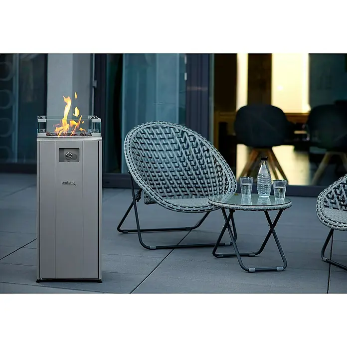Feuersäule - L x B x H: 37,1 x 37,1 x 94,8 cm, Anthrazit - Ein moderner Gas-Terrassenheizer mit Glasaufsatz, daneben Korbstühle und ein Tisch mit Getränken. Perfekt für gemütliche Abende im Freien.