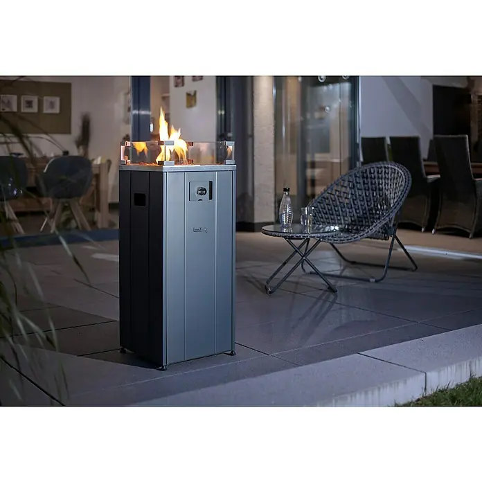 Feuersäule - L x B x H: 37,1 x 37,1 x 94,8 cm, Anthrazit - Blick auf eine stilvolle Gasfeuerstelle mit Glasumrandung auf einer Terrasse, daneben ein Tisch mit Stuhl und eine Sitzecke im Hintergrund.