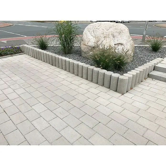Diephaus Kleinpalisade - Ø x H: 15 x 60 cm, Grau, Beton - Eine gepflasterte Fläche mit rechteckigen Pflastersteinen und einer runden Beetbegrenzung aus Beton. Der Weg führt an einem Steingarten vorbei.