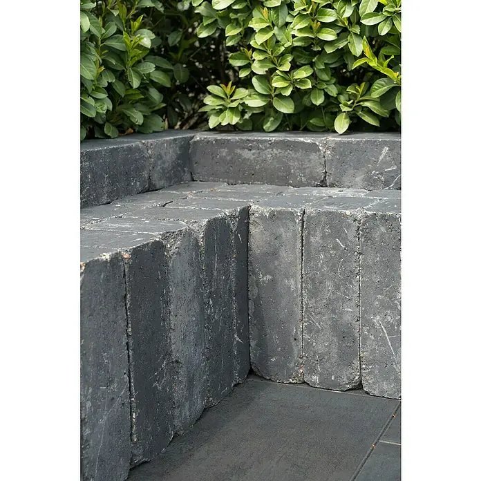 Diephaus Mauerstein Austin - 30 x 20 x 10 cm, Basalt, Beton - Nahaufnahme eines grauen, aus Ziegeln gefertigten Blumenkastens im Freien mit grünen Pflanzen im Hintergrund.