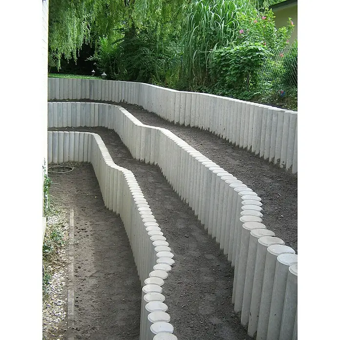 Diephaus Rundpalisade - 20 x 120 cm, Grau, Beton - Aufnahme einer mehrstufigen Gartenlandschaft mit Betonpfosten, die als dekorative und funktionale Stützmauer dienen.