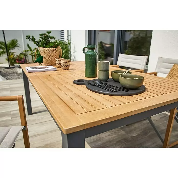 Sunfun Carina Gartentisch - L x B x H: 180 x 100 x 75 cm, Akazie, Stahl, Rechteckig, Hellbraun - Ein Outdoor-Esstisch mit heller Holzlattenplatte und dunkelgrauem Gestell, auf einer Terrasse mit Stühlen und Geschirr.