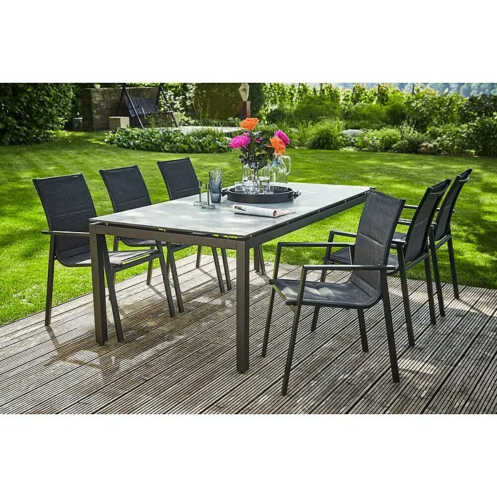 Sunfun Melina Gartensessel - Aluminium, Textilen, Stapelbar, Schwarz, B x T x H: 56,5 x 66 x 91 cm - Ein Gartentisch-Set mit sechs Stühlen auf einer Holzterrasse, umgeben von grünem Rasen und Büschen, ideal für Mahlzeiten im Freien.
