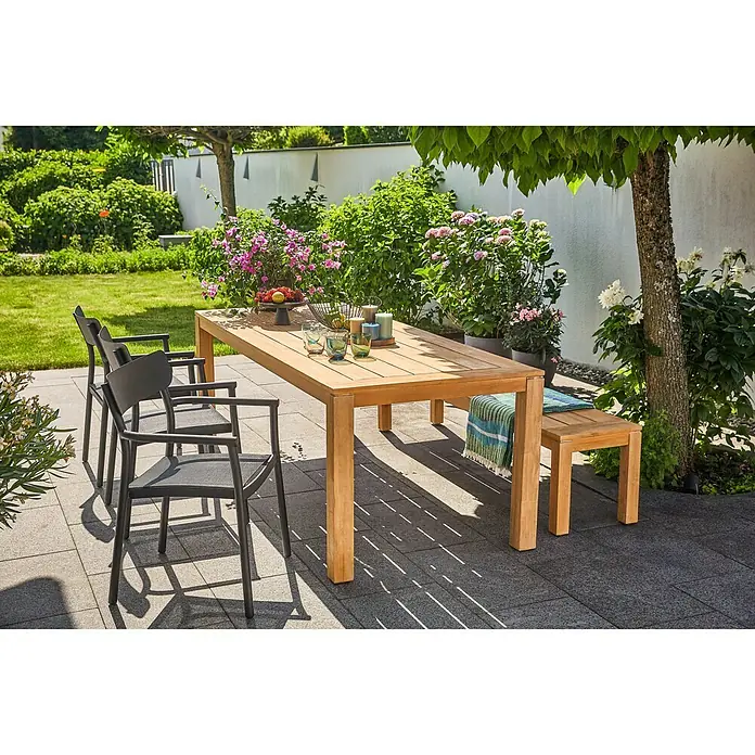 Sunfun Laura Gartenbank - B x T x H: 190 x 42 x 45 cm, Akazie, Naturbraun - Eine hölzerne Gartentischgruppe mit Stühlen und Bank auf einer gepflasterten Terrasse, umgeben von üppigem Grün.