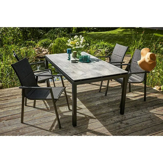 Sunfun Melina Gartentisch - L x B x H: 160 x 90 x 74 cm, Aluminium, HPL, Rechteckig, Schwarz - Ein grauer Gartentisch mit vier Stühlen steht auf einer Holzterrasse, dekoriert mit Blumen und Gläsern, perfekt für entspannte Stunden im Freien.