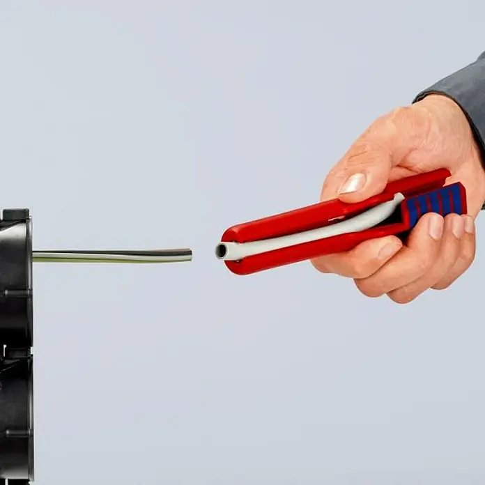 Knipex Pelacable - Largo: 17,5 cm - Una mano utiliza una herramienta de pelado de cables KNIPEX roja para pelar un cable que sale de una caja de conexiones negra.