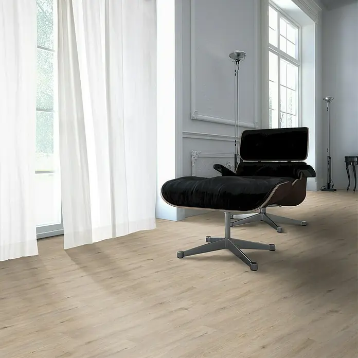 Fixed Vinylbodenmuster - Eiche Cream, 280 x 160 x 2,5 mm, Landhausdiele - Moderner Sessel mit Fußhocker in einem hellen Raum mit großen Fenstern und weißen Vorhängen. Elegantes Design und komfortable Sitzgelegenheit.