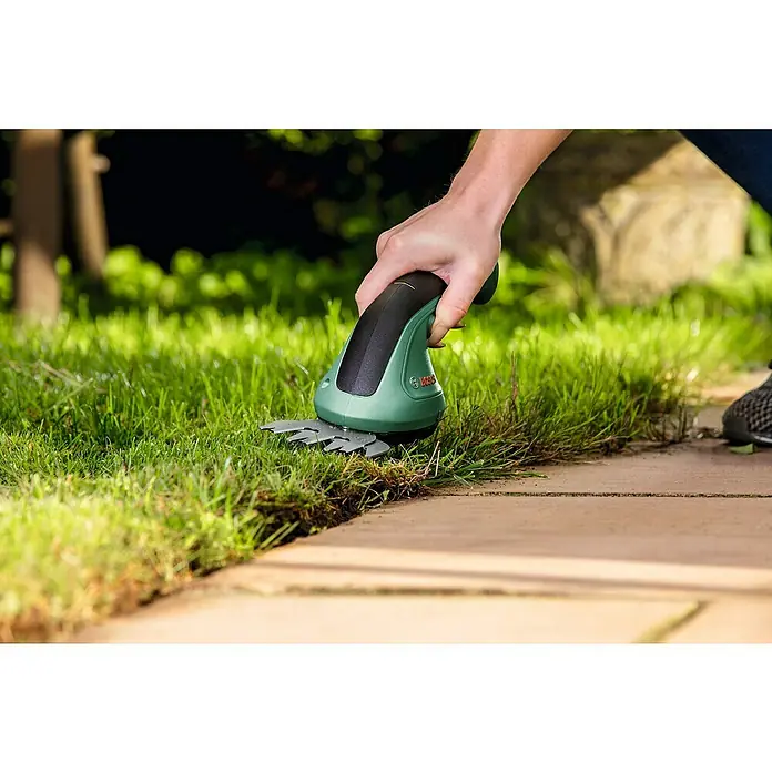 Bosch Podadora de batería EasyShear - 3,6 V, Iones de litio, 1 batería, Anchura de la hoja: 8 cm - Una persona usa unas tijeras de césped inalámbricas Bosch para bordear el césped a lo largo de un camino pavimentado.