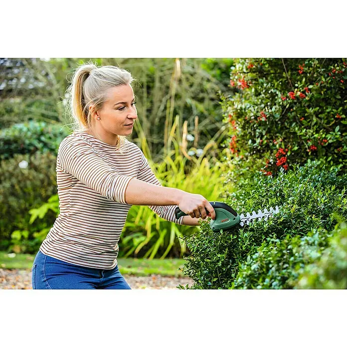 Bosch Podadora de batería EasyShear - 3,6 V, Iones de litio, 1 batería, Anchura de la hoja: 8 cm - Una mujer está usando una tijera para arbustos sin cable Bosch para recortar un seto. La tijera para arbustos sin cable permite una jardinería precisa.
