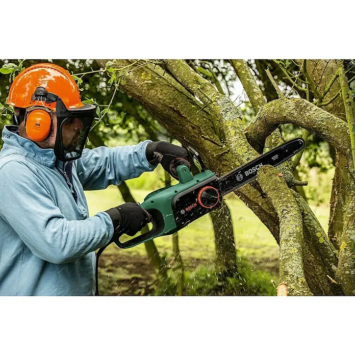 Bosch Elektro-Kettensäge UniversalChain 40 - 1.800 W, Schwertlänge: 40 cm - Ein Mann schneidet mit einer Bosch Kettensäge einen Baum. Er trägt Schutzkleidung für die Arbeit im Garten, um sicher zu arbeiten.