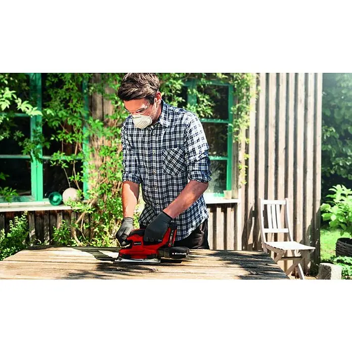Einhell PXC 18V Lijadora orbital de batería TE-OS 18/230 Li-Solo - 18 V, Sin batería, 14.000 r.p.m. - 24.000 r.p.m. - Un hombre usa una lijadora Einhell al aire libre para trabajar la madera, con gafas de seguridad y mascarilla antipolvo.