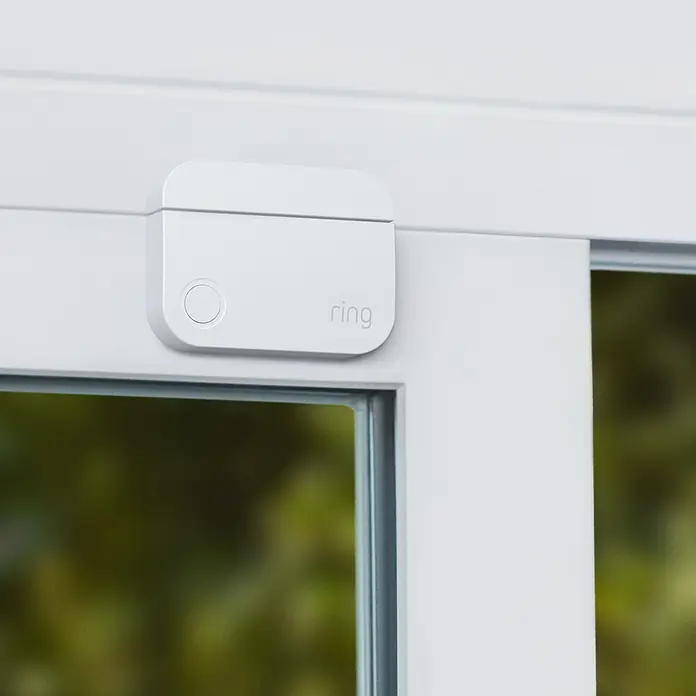 Ring Alarm Sicherheit Starter-Paket 5-teilig 2. Gen. - Smarte Steuerung: Ring App - Nahaufnahme eines Ring-Alarmsensors an einem weißen Fensterrahmen, der ein Gefühl von Sicherheit und moderner Technologie vermittelt.