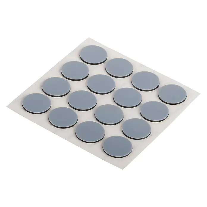 Suki Patín antideslizante para alfombras - Diámetro: 17 mm, Gris, 16 ud. - Esta imagen muestra una lámina de deslizadores redondos grises para muebles con parte posterior autoadhesiva. Los deslizadores están ordenados en la lámina.